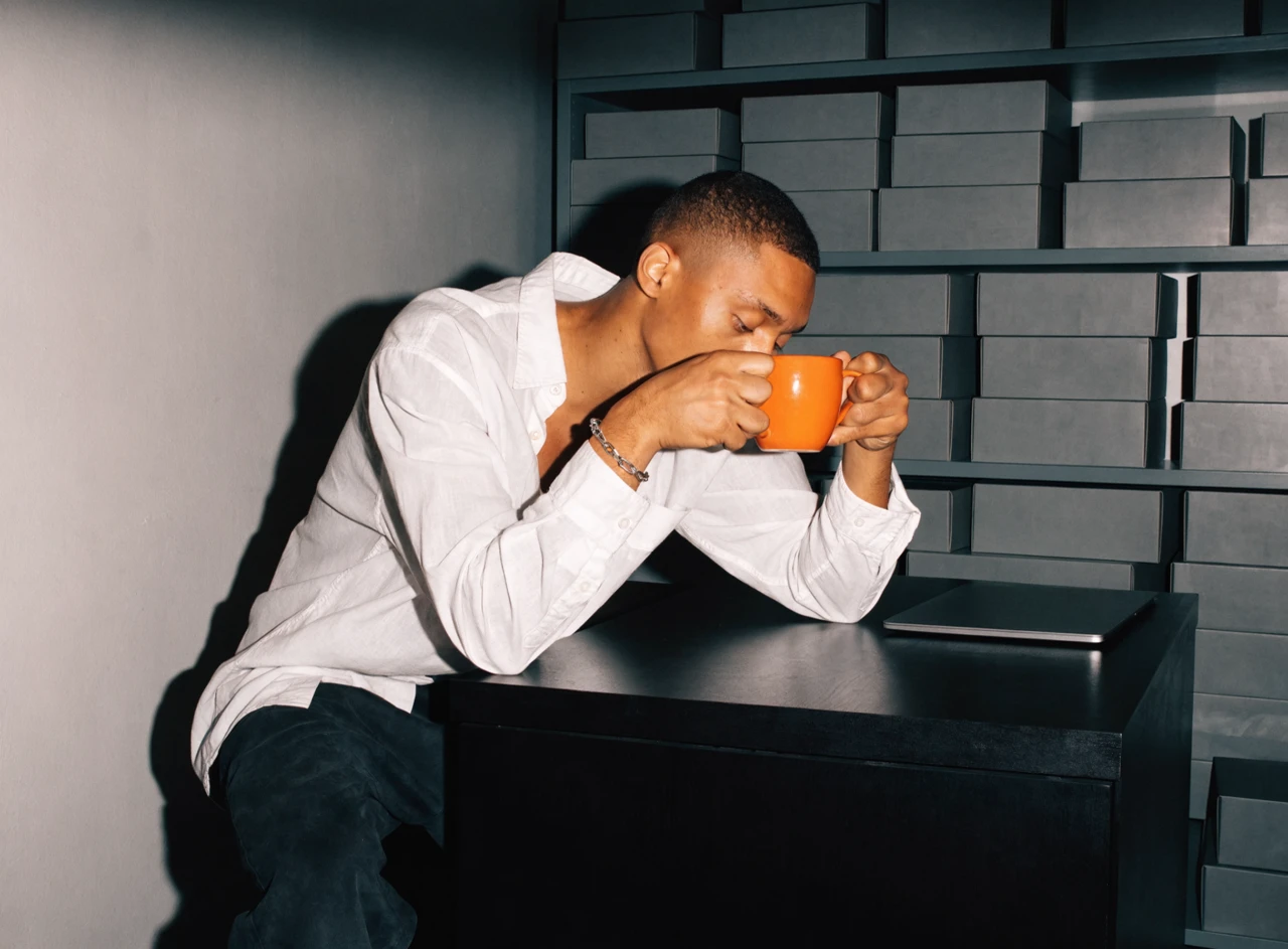 Person calmly drinking from an orange mug in a tidy stockroom